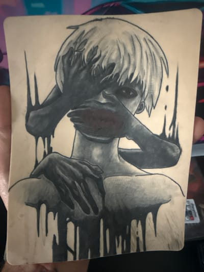 A grayscale drawing on a textured, light-colored surface depicts a stylized humanoid figure with short, spiky white hair. The figure's face is obscured by two dark-skinned hands. One hand covers the eyes, while the other covers the mouth, with a hint of red visible beneath it, suggesting lips. The figure's body is rendered with shading, showing a bare chest and shoulders. Dark, viscous-looking lines drip down from the figure's shoulders and head, creating a distressed or melting effect. The background is a solid, light color. The image is held by a person whose hand is visible on the left side. The setting is not discernible from the image itself and no city or location can be identified.