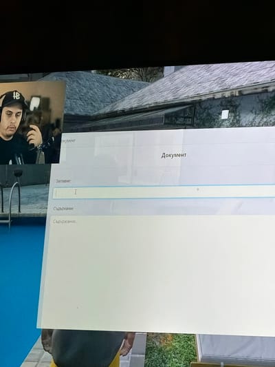 The image shows a close-up of a computer screen displaying a document creation interface. On the left side of the screen, a man wearing a black baseball cap with a white logo and headphones is visible, seemingly reacting to something on the screen. The interface shows fields for "Document," "Title," and "Content." The title field contains the letter "I." The background of the screen displays a blurred image of a house with a gray roof and some greenery. The lower part of the screen shows a bright blue surface, likely a swimming pool, and a person's legs wearing yellow and dark clothing. The provided context mentions Graf Ignatievo, Bulgaria, but this location is not visually identifiable within the image itself.