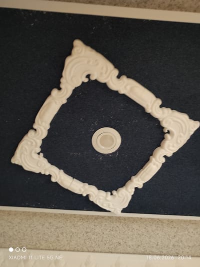 An ornate, white ceiling trim piece, likely made of plaster or a similar decorative material, is centered against a dark blue textured background. The trim is shaped like a stylized diamond with elaborate scrollwork and flourishes at each corner. In the center of the diamond shape, a white circular light fixture is visible, recessed into the ceiling. The overall composition is a close-up, overhead view. The image also displays a timestamp in the lower right corner that reads "18.06.2026 20:14" and a device model indicator "XIAOMI 11 LITE 5G NE" in the lower left. There is no information in the image to suggest a specific location in the city of Böblingen, Germany.