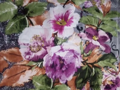The image presents a floral pattern on fabric. Predominantly, large blooms in shades of white, pink, and purple dominate the scene. Green leaves, interspersed amongst the flowers, add contrast. Brown and beige-toned elements are visible in the leaf details. A grey, textured background complements the vibrant floral arrangement. The overall impression is a decorative and colorful textile design.