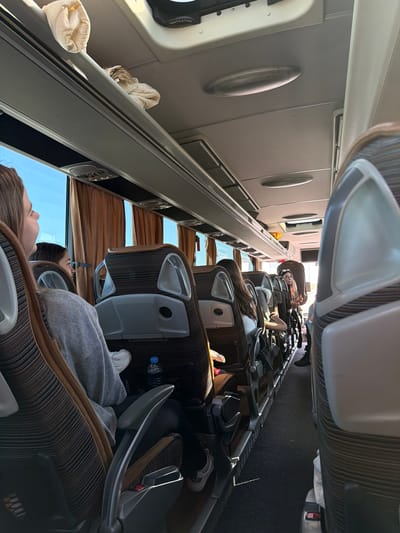 The image depicts the interior of a bus with passengers. The seating arrangement is rows of upholstered chairs. People are seated, some appearing to be resting. The bus windows have curtains, and the landscape visible outside suggests daylight. The interior lighting is soft. The image doesn't give information regarding the location. It is not possible to determine the location in the city of Malko Tranovo, Bulgaria, with the available context.