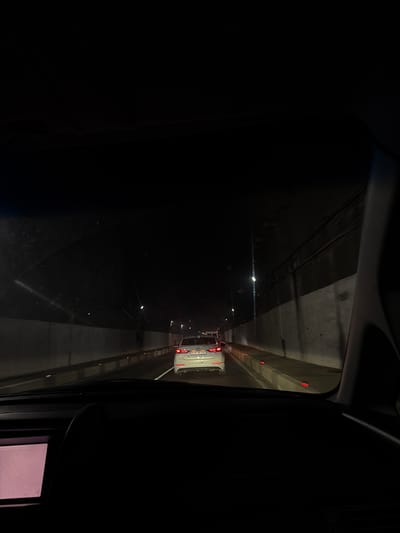 The image shows a view from inside a vehicle driving through a tunnel. A white car is visible in the lane ahead. The tunnel walls are concrete, with overhead lighting. The location is not identifiable as Semyonovka, Armenia from the given image.