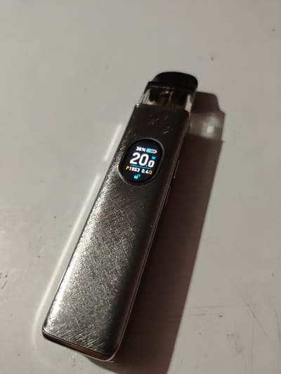 A silver vape device with a black mouthpiece is positioned on a white, speckled surface. The device has a digital display showing "36%", "20.0W", and "P1953 0.4Ω" along with a padlock icon. The surface appears to be a table or countertop. A shadow of the vape device is cast to the right. The scene is devoid of any context related to Akhmetovskaya, Russia, and no people are present.