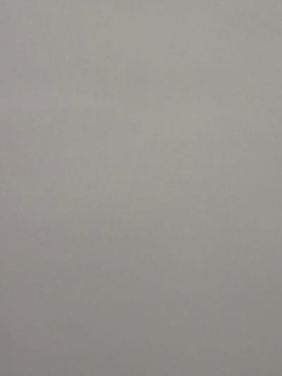 The image displays a uniform, muted medium-gray surface, exhibiting a subtle, fine-grained texture across the entire frame. The texture is consistent with either a non-reflective paper or a flat textile material. No specific features, patterns, or anomalies are discernible within the frame, indicating an even surface and consistent lighting conditions. There are no visible people, subjects, objects, actions, or interactions. The environmental context is limited to this uniform surface. This scene is located in Kubrat, Bulgaria.