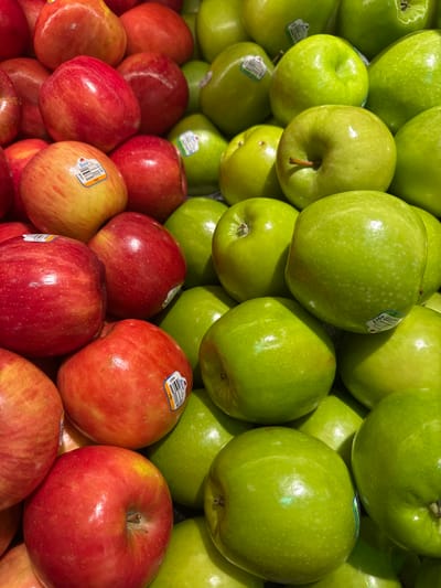 A close-up, overhead shot of a pile of red and green apples. The apples are arranged in a disorganized manner, filling the frame. Some of the apples have stickers on them with barcodes and text such as "USA" and "Fuji." The lighting is bright and even, highlighting the smooth surfaces and vibrant colors of the fruit. The image does not contain any discernible information that would allow for the identification of a specific location in Shaker Heights, United States of America, nor does it depict any people or actions.
