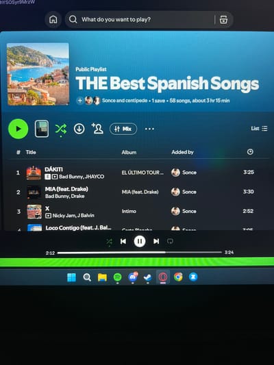 The image shows a computer screen displaying the Spotify application. The playlist titled "THE Best Spanish Songs" is open. The playlist features several songs, including "DÁKITI" by Bad Bunny and Jhayco, "MIA (feat. Drake)" by Bad Bunny and Drake, and "X" by Nicky Jam and J Balvin. The playlist was added by "Sonce". The playback progress bar indicates that the current song is at 2:12 and the total duration of the song is 3:24. The application is running on what appears to be a Windows operating system, as indicated by the taskbar icons at the bottom of the screen, which include the Windows logo, a search icon, a folder icon, the Spotify icon, and other application icons. There is no visible indication that this scene is located in Verden (Aller), Germany.