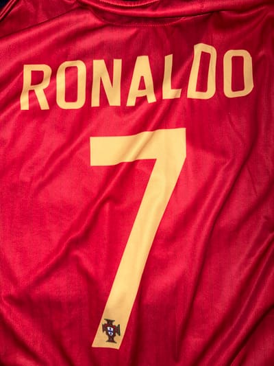 The image shows a close-up, top-down view of a red soccer jersey with "RONALDO" printed in gold block letters across the top, followed by a large gold number "7" below it. A small crest, the Portuguese coat of arms, is visible at the bottom left corner of the number 7. The jersey is made of a textured fabric with subtle vertical ribbing and is creased in several places due to being laid flat. There are no people, interactions, or environmental details visible, and the location in Nikopol, Bulgaria, is not indicated in the image itself.