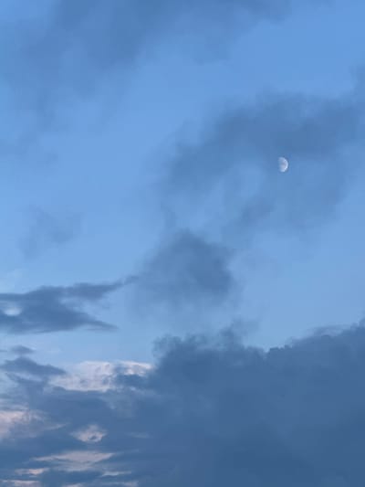 A photograph captures a dusky sky with a waxing crescent moon visible on the left side of the frame. Dark, wispy clouds dominate the scene, creating a dramatic backdrop of various shades of blue and gray. The clouds are dense and textured, with some areas appearing lighter and more diffused, while others are thick and imposing. The moon, a small, pale sliver, stands out against the darker clouds, hinting at the transition from day to night.
The lighting suggests it is either early morning or late evening, with the sun not fully present, allowing the moon to be seen. The overall mood is serene yet somewhat mysterious, with the cloud formations adding a sense of depth and movement to the sky. There are no visible people or objects within the frame, and no text is present. The setting is an outdoor sky view, possibly from a location in Gamovo, Russia, given the provided context, suggesting a peaceful, natural environment. The weather appears to be partly cloudy, with the potential for a clear night ahead.