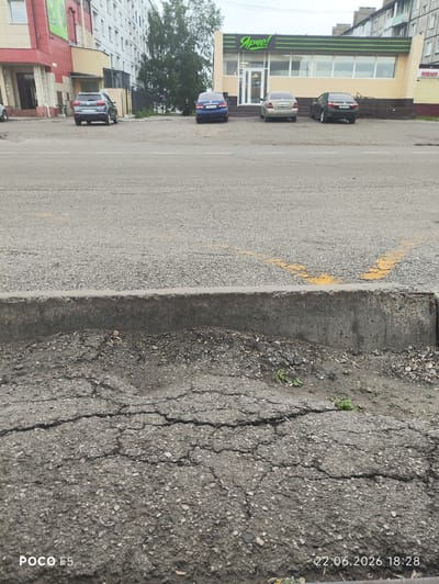 The image shows a street in Kaltan, Russia, with several cars parked in front of a commercial building. The building has a prominent sign that reads "Ярче!". The street is paved with asphalt, and there is a concrete curb separating the road from a patch of dirt and gravel. The weather appears to be overcast. The image also has a watermark at the bottom left corner that reads "POCO F5" and at the bottom right corner that reads "22.06.2026 18:28".