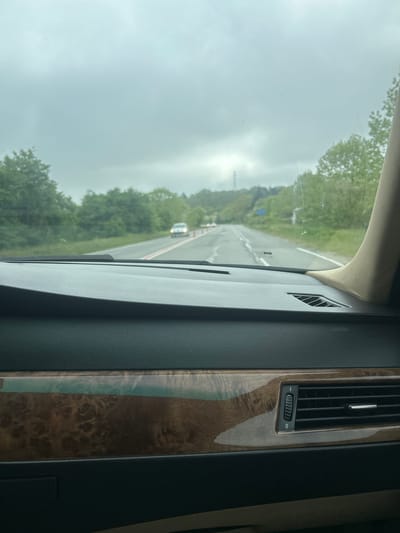 The image shows a view from inside a car, looking out onto a road. The road appears to be a two-lane highway, passing through a forested area. The sky is overcast and grey. The car's dashboard is visible in the foreground, featuring dark grey upholstery and a wood-grain trim with an air vent. There are no visible people. While the location provided is Staro Oriahovo, Bulgaria, there are no specific details in the image to confirm this.