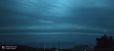 The image depicts a dark, cloudy sky with distinct horizontal cloud formations, possibly indicating turbulent weather or atmospheric layering. In the foreground, silhouetted against the sky, are the dark shapes of trees and buildings, suggesting a rural or suburban landscape at dusk or under heavy cloud cover. The presence of a Redmi Note 9 Pro watermark in the bottom left corner indicates the image was captured by this device. The location is identified as Mliiv, Ukraine. There are no visible people or specific actions taking place in the scene. The overall atmosphere is somber and potentially foreboding due to the dark lighting and stormy sky.
