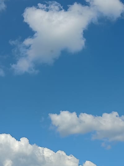A bright blue sky dominates the image, with several white, puffy clouds scattered throughout. In the upper portion of the frame, a large cloud formation is prominent, while smaller clouds are visible in the lower half. The sky appears clear, suggesting fair weather. There is no discernible indication of the city of Gukovo, Russia, or any specific landmarks within the image. No people, objects, or actions are depicted; it is a simple landscape photograph of the sky.