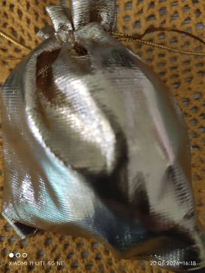 A close-up, vertical shot captures a silver drawstring gift bag, its metallic surface reflecting light and creating highlights and shadows. The bag is positioned on a textured, woven surface, likely a fabric or mat, which appears to be yellow or light brown. The drawstring, also metallic, is visible at the top of the bag, cinched to close it. The background consists of this textured material, filling the frame around the bag. In the bottom left corner, a watermark reads "XIAOMI 11 LITE 5G NE," and in the bottom right corner, a date and time stamp reads "20.06.2026 16:18." There are no people or any clear indications of the location being Böblingen, Germany.