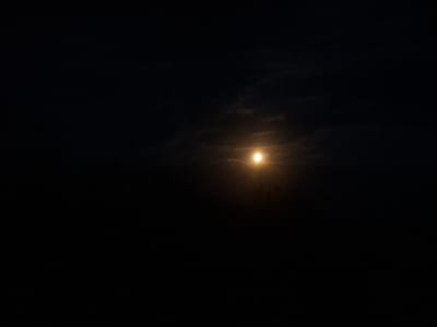 This image shows a dark sky with a bright, round object in the center, which appears to be the moon. The moon is partially obscured by clouds, which are also dark and wispy. The overall impression is one of nighttime. There is no indication of the city of Chorna, Ukraine, or any other specific location. There are no people, subjects, objects, or actions visible in the image.