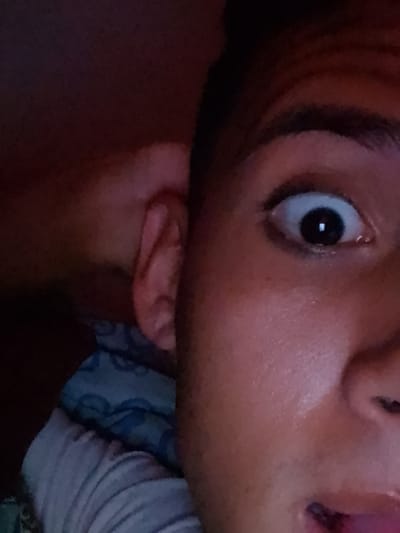 The image shows a close-up of a person's face in a state of surprise, with their eye wide open and mouth slightly agape. The person is lying on a pillow with a blue and white patterned case. Part of the person's ear is visible, along with their nose and eyebrow. The background is dark. The image was taken indoors. There is no information available to identify the location as El Espinal, Venezuela.