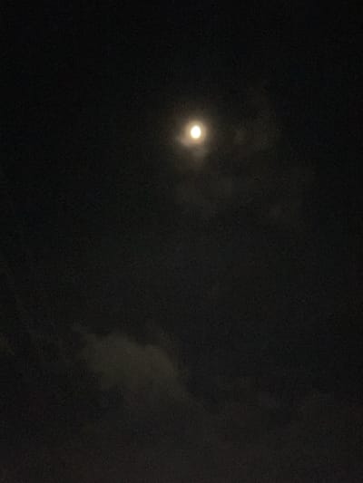 The image depicts a night sky with a visible moon. The moon is luminous and slightly diffused, suggesting the presence of thin clouds or haze in the atmosphere. Dark clouds are scattered across the frame, obscuring parts of the sky. The overall scene is dark, characteristic of nighttime. The location is specified as Landuh, Indonesia. There are no people, animals, or man-made structures visible in the image. The image appears to be a photograph taken outdoors.