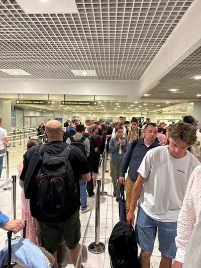 The image depicts a queue of people at what appears to be an airport in Surcin Urban Municipality, Serbia, likely at the passport control or baggage claim area, based on the signage in the background. The environment is indoors, with a modern, grid-patterned ceiling and fluorescent lighting. Several individuals are standing in line, many are carrying backpacks and luggage. Some are looking at their phones, while others are looking forward. The overall scene suggests a typical travel waiting situation.