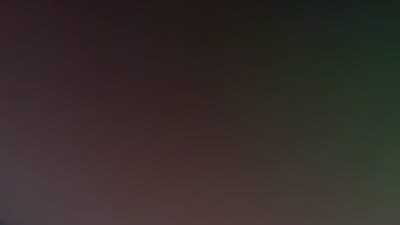 The image presents an abstract, dark, and smooth color gradient, with no discernible subjects, people, or objects. The primary colors transition from a deep, muted reddish-brown or dark maroon on the left and central parts of the frame, gradually blending into a dark, desaturated olive green or forest green towards the right side. A very subtle hint of dark blue or purple is present in the extreme bottom-left corner. A single, tiny, faint white speck can be observed in the lower-right quadrant.

The overall impression is one of low light, suggesting a dim environment, possibly nighttime. There are no activities or events taking place within the frame, nor are there any specific location cues visible. No text is present in the image. While the provided location context is Umarevtsi, Bulgaria, this information cannot be discerned from the visual content itself.