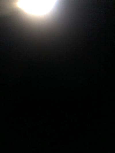 The image is predominantly black, with a bright, circular light source in the bottom left corner. The light diffuses upwards, creating a gradient effect across the lower-left portion of the image. The remaining area is dark, devoid of visible details or shapes. The overall composition evokes a sense of darkness, punctuated by a strong light source.