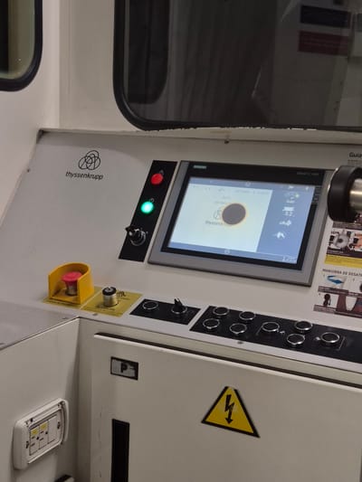 The image shows a close-up of the control panel of an industrial machine. The panel is white with a touchscreen display labeled "SIMATIC HMI TOUCH," manufactured by Siemens. The screen displays system information and a Thyssenkrupp logo. The panel also features various buttons, switches, indicator lights (red and green), a prominent emergency stop button with a yellow guard, an electrical outlet, and a high-voltage warning symbol. The location information, "Rionegro, Colombia," is not discernible from the image.