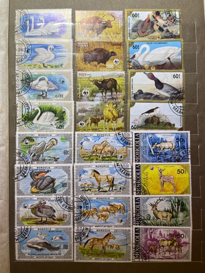 The image displays a collection of postage stamps, arranged in a grid. Each stamp features an illustration of various animals and natural scenes, predominantly wildlife from Mongolia. The stamps show swans, pelicans, deer, horses, and wild oxen. The condition of the stamps appears to be good, with visible perforation lines separating them. Some stamps have postmarks indicating they are from Mongolia, with denominations in "mongol shuudan" and dollar cents. The stamps are mounted on a grey backing material, possibly an album page. The overall scene is of a philatelic collection. There is no discernible relation to Kramatorsk, Ukraine; the image depicts only stamps.