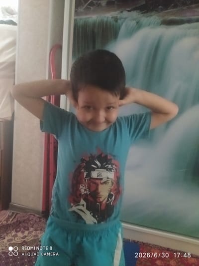 The image shows a young boy lying down, with his arms behind his head. He is wearing a blue t-shirt with a graphic print of a character from the anime "Naruto". The background appears to be a wall with a large, abstract painting or tapestry featuring swirling patterns of blue, white, and green. The boy's expression is relaxed, suggesting he is at ease in a domestic setting, possibly his home. The image is a photograph, and the lighting is soft, indicating it might have been taken indoors during the daytime. The bottom right corner of the image contains text: "2026/6/30 17:48" and "REDMI NOTE 8 AI QUAD CAMERA". The timestamp suggests the image was taken in the late afternoon. The overall scene conveys a sense of casual leisure.