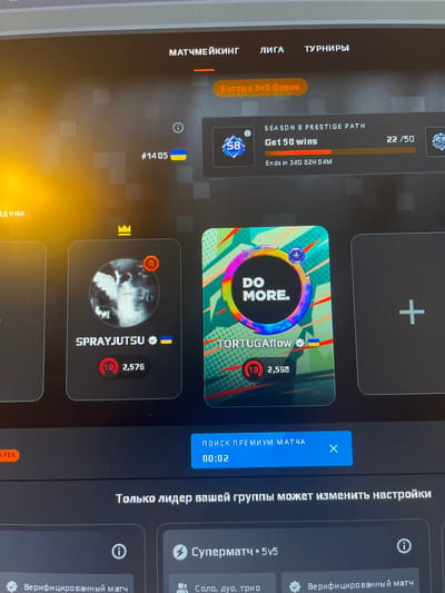 The image shows a computer screen displaying a gaming interface, likely for a competitive online game. The interface features game modes, player profiles, and statistics. In the foreground, a blue button with white text reads "ПОИСК ПРЕМИУМ МАТЧА" (Search for premium match) and a timer "00:02". Below this, text in Russian states "ТОЛЬКО ЛИДЕР ВАШЕЙ ГРУППЫ МОЖЕТ ИЗМЕНИТЬ НАСТРОЙКИ" (Only the leader of your group can change settings). Further down, there are options for "Суперматч • 5v5" (Supermatch • 5v5) and "Верифицированный матч" (Verified match).
Player cards are visible on the screen. One card displays "SPRAYJUTSU" with a profile picture and a rank of (10) 2,576. Another card shows "TORTUGAflow" with a similar rank of (10) 2,598 and a profile picture with the text "DO MORE.". There is also a progress bar indicating "SEASON 8 PRESTIGE PATH" with "Get 50 wins" and a current count of "22/50".
The top of the screen shows menu items in Russian: "МАТЧМЕЙКИНГ" (Matchmaking), "ЛИГА" (League), and "ТУРНИРЫ" (Tournaments).
There is no information in the image that would suggest its location in the city of Pobiedziska, Poland.