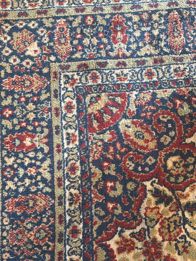 This is a close-up, overhead shot of a richly patterned carpet in Byurakan, Armenia. The carpet features a complex design with recurring floral and geometric motifs in shades of deep blue, red, gold, and green. The texture appears plush and woven. The specific location in Byurakan, Armenia, is not visible in the image.