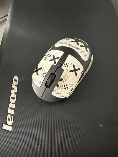 A computer mouse is situated on a black Lenovo laptop. The mouse is white with a pattern of black "X"s and plus signs. The laptop is in Новоглаголево, Russia.