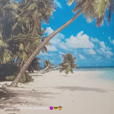 The image depicts a tropical beach scene with palm trees, white sand, and a blue sky with clouds. The ocean is visible in the background. In the foreground, the text "найди меня если сможешь" is overlaid, which translates to "find me if you can". This text is accompanied by three emojis: a devil face, sunglasses face, and a cowboy face. There are no people or recognizable landmarks present in the image. The scene is not located in Pskov, Russia, as the environment is clearly tropical and not representative of that region.