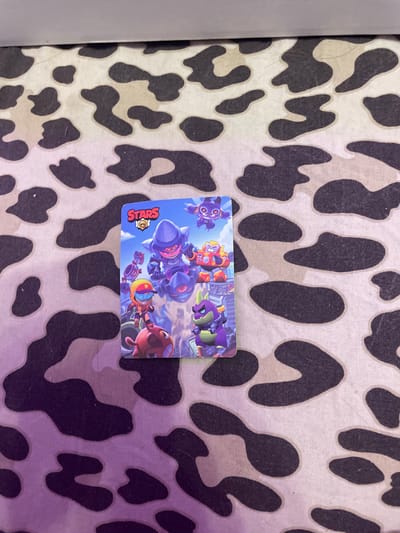 A Brawl Stars card featuring several characters is placed on a black and white cow-print surface. The card is positioned towards the left side of the frame, slightly angled. The background surface appears to be a mat or fabric. There are no discernible city landmarks or indications of Vaganovo Massiv, Russia, in the image.