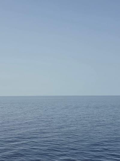 The image depicts a serene seascape with a clear, pale blue sky meeting a calm, deep blue ocean at the horizon. The water's surface is gently rippled, suggesting a tranquil atmosphere. The scene is devoid of any human presence or man-made objects, presenting a vast expanse of natural elements. The location is identified as Santa Ponça, Spain, a coastal town known for its beaches and marina. The photograph captures the essence of a peaceful day at sea, highlighting the simplicity and immensity of the ocean and sky.