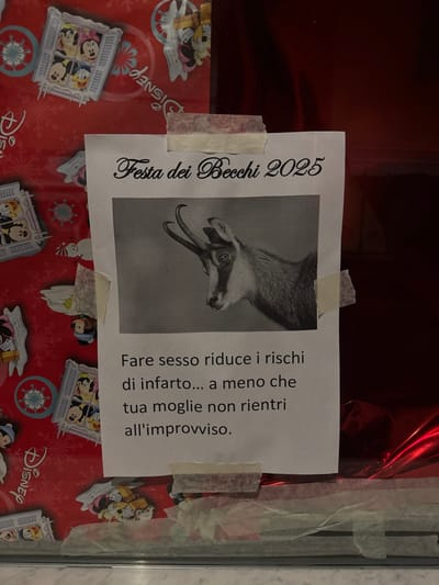 The image shows a sheet of paper taped to a surface with Disney-themed wrapping paper. The paper features an image of a goat and the text "Festa dei Becchi 2025." Below the image, text reads "Fare sesso riduce i rischi di infarto... a meno che tua moglie non rientri all'improvviso," which translates to "Having sex reduces the risk of a heart attack... unless your wife comes home unexpectedly." It appears to be an invitation or advertisement for a party with a humorous message.