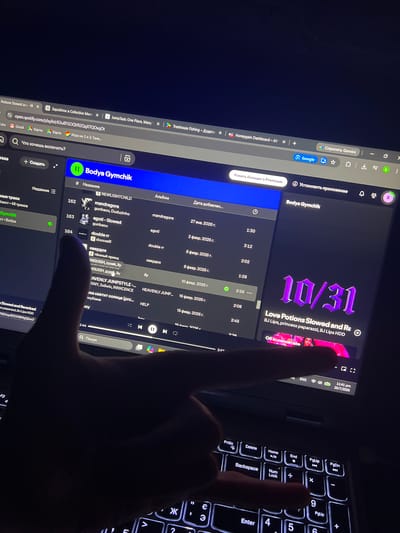 The image depicts a person's hand interacting with a laptop screen, which displays a Spotify playlist titled "Bodya Gymchik". The playlist contains various songs with their corresponding artists and album information. Some song titles and artists visible include "mandrapora", "agoti - Slowed", "double rr", and "ОВЕРДОЗ". The time and date displayed on the laptop are "11:41 pm 20/7/2026". The environment appears to be indoors, with the laptop screen being the primary light source. There are no discernible geographical landmarks or elements that would suggest a specific location within the city of Sobishchytsi, Ukraine.