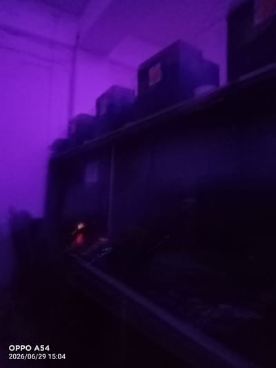 The image captures a dimly lit interior space, likely a room or storage area, with a dominant purple hue cast by artificial lighting. In the background, a shelf or raised surface holds several dark, rectangular objects, possibly boxes or equipment. The lighting creates long shadows, obscuring many details. In the lower part of the image, there is a faint reddish glow, suggesting a light source or perhaps a reflection. A diagonal beam of purple light cuts across the lower right section of the frame. The overall mood is somewhat mysterious and indistinct due to the low light and the color saturation.
Visible text in the bottom left corner reads "OPPO A54" and "2026/06/29 15:04", indicating the phone model used to capture the image and the date and time it was taken. The date is in the future, which might suggest it's a placeholder or an error in the timestamp. The setting does not provide specific cues to Bokhtar, Tajikistan, beyond what is provided in the prompt. The time of day, 15:04, would typically be afternoon, but the artificial lighting makes it difficult to ascertain natural light conditions. No people or clear activity are depicted.