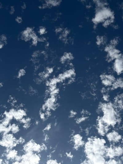 The image shows a daytime sky in Bonhill, United Kingdom. The sky is a deep blue color, with scattered white clouds of varying sizes and shapes. The clouds appear to be altocumulus, arranged in sheets or layers at a mid-altitude. There are no people, subjects, or objects visible in the image other than the sky and clouds. No actions or interactions can be determined from the picture. The environment is a clear day with some cloud cover.