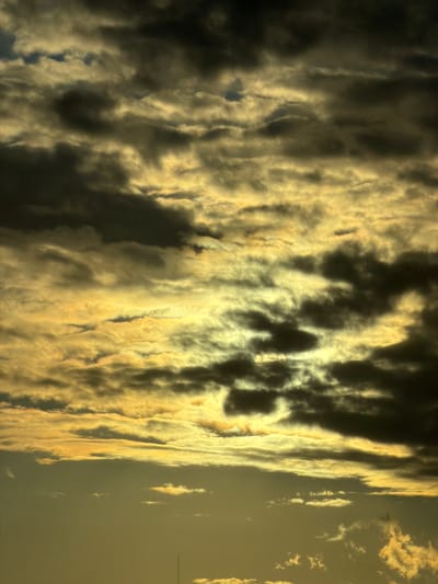 This is a photograph of a cloudy sky above the city of Kopaniny, Poland. The clouds are dark and heavy, with streaks of golden light shining through them. The overall atmosphere of the image is dramatic and moody. There are no people or specific objects visible in the scene, other than the clouds and the sky. The image appears to be taken during daylight hours, likely at sunrise or sunset, given the dramatic lighting.