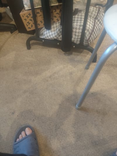 The image shows a close-up of a person's left foot wearing a blue slide sandal. The foot is resting on a carpeted floor. In the background, a metal-legged stool or table is visible, along with a patterned bag and a box with a butterfly pattern. The scene appears to be indoors, likely a residential setting. The location in Furmanov, Russia, is not depicted or suggested by the image content.