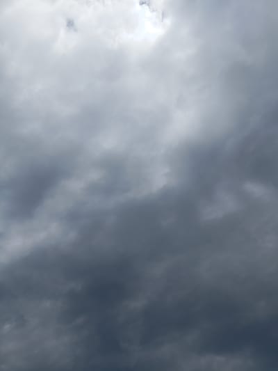 This is a low-angle, full-frame photograph of an overcast sky filled with dense, dark grey clouds. There are a few brighter patches towards the top of the image where the sun is attempting to break through. The clouds are textured and layered, suggesting a potentially stormy or cloudy day. The image appears to be taken outdoors, looking upwards, and there are no people, subjects, or objects visible in the frame. The location is not identifiable from the image itself.