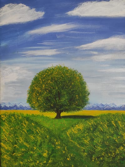 This is an acrylic painting on canvas depicting a solitary, full-bodied green tree with yellow blossoms standing in a vibrant green field dotted with yellow flowers. In the background, a strip of yellow horizontal expanse is visible, possibly a field of crops, behind which a range of blue, mountainous terrain is depicted. The sky is a bright blue, filled with scattered white clouds painted with visible brushstrokes. The painting captures a serene, rural landscape, possibly inspired by the natural beauty of Kipshek, Russia. There are no people or animals present in the scene.