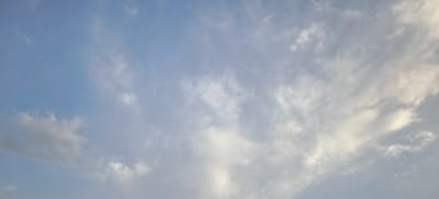 The image shows a sky with scattered clouds over Margilan City, Uzbekistan. The clouds are a mix of white and grey, with some areas appearing wispy and translucent. The sky is a pale blue, suggesting it might be morning or late afternoon. There are no people, objects, or specific landmarks visible that would indicate a precise location within the city. The scene is serene and natural, focusing solely on the atmospheric conditions.