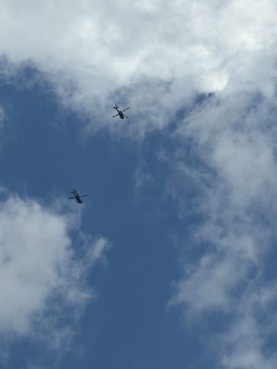Two helicopters are visible in the sky, silhouetted against a blue sky with scattered clouds. The helicopters appear to be military or civilian aircraft, with a distinct rotor system. The lower helicopter is closer to the camera, while the upper helicopter is further away and slightly to the right. The image does not provide any specific details about the location within the city of Zlati Voyvoda, Bulgaria.
