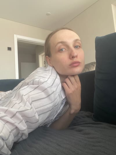 A person is reclining on a couch. The person is wearing a striped shirt and has their hand near their neck. The background includes a wall and a door frame. The location is not identifiable as Sepych, Russia from the image.