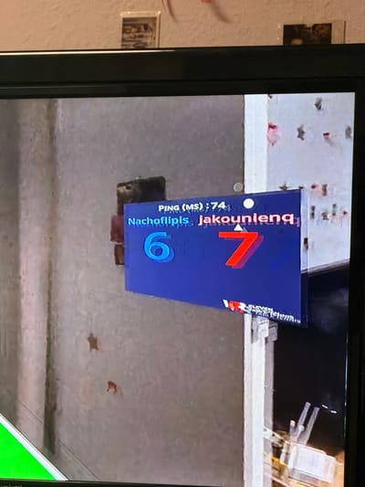 The image shows a close-up of a television screen displaying a score in a video game. The score shows one player, "Nachoflipis," with 6 points, and another player, "jakounienq," with 7 points. The game appears to be tennis, as indicated by the text "ELEVEN TABLE TENNIS" visible at the bottom of the screen. The background of the image is a textured wall, likely in a room. There is no information in the image to suggest the location is Castillo Bajo-conejito, Spain.