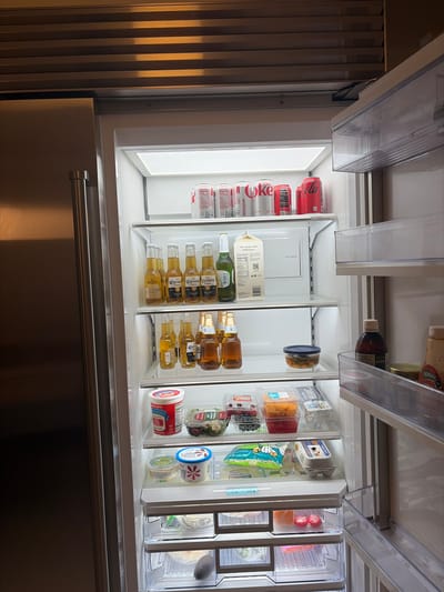 Detailed analysis of the open refrigerator reveals a variety of food and beverage items neatly arranged on the shelves. The leftmost shelf contains numerous cans of Diet Coke. Adjacent to this shelf is a selection of items including a carton of Maple Hill Organic milk, several bottles of Corona Extra beer, and a mix of clear and amber-colored bottles. The rightmost shelves display assorted containers with yogurt, cheese, fruits, and salads. Above the shelves are additional containers and bottles.
The location is not specified or indicated by the visual information, and therefore any claims of it being in the city of Key Biscayne, United States of America or any other location is not supported by the provided image.