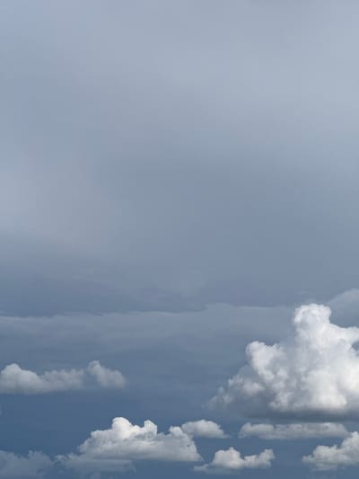 This vertically oriented image captures a serene daytime sky. The left side of the frame is largely filled with a uniform, soft blue-grey expanse, which appears slightly hazy or diffused. As the eye moves towards the right, the sky transitions to a brighter, clearer blue, punctuated by a series of distinct, fluffy white cumulus clouds.

The clouds are varied in their formation, with some appearing as large, dense masses and others as smaller, scattered wisps along the right edge and extending into the mid-right section of the frame. Their bright white appearance suggests strong illumination by sunlight, indicating it is daytime. There are also subtle streaks or layers of thinner cloud visible, adding textural depth against the blue backdrop.

No people, man-made objects, or specific events are depicted in the image; it is purely a natural scene of the sky and its cloud formations. There are no visible textual elements. The overall impression is one of calm, with a mix of clear and cloudy conditions. The image does not contain any specific visual cues to identify a location within Barnsley, United Kingdom.
