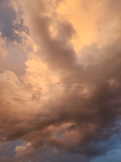 The image shows a dramatic sky filled with large, billowing clouds, predominantly in shades of orange, yellow, and gray. Some parts of the clouds are illuminated by warm, golden light, suggesting a sunset or sunrise. Other areas are darker and more ominous, with hints of blue sky peeking through in the lower portions. There are no people, structures, or identifiable landmarks in the image, only the expansive sky. The location is identified as Winter Park, United States of America.