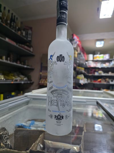 The image shows a bottle of "Hetman" premium vodka lying horizontally on what appears to be a refrigerated display case in a store. The bottle is frosted and labeled in Ukrainian. The background is blurred, suggesting the inside of a retail establishment, possibly a liquor store. Shelves of bottled goods can be seen in the background. There is no evidence to support this image being taken in Pripek, Bulgaria.