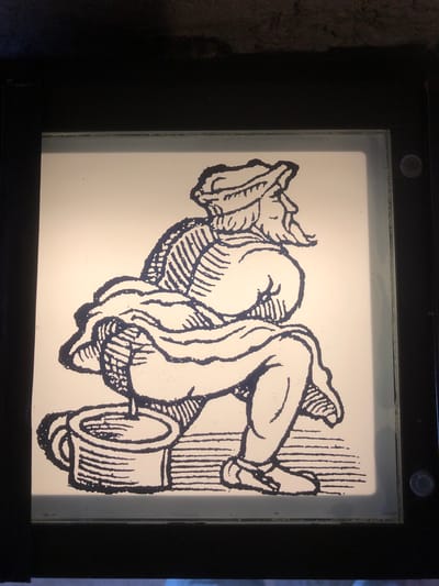 The image shows a black and white cartoon of a person lying on a toilet paper roll next to a pole, encased within a black frame on a white lightboard. This image can be found within the city of Veytaux, Switzerland.