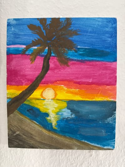 This is a painting of a tropical beach at sunset. The sky is a gradient of colors, from deep blue at the top to pink, orange, and yellow at the horizon. A large palm tree with dark brown fronds leans over the scene from the left. The sun, a bright yellow circle, is low on the horizon, casting a reflection on the deep blue water. The beach in the foreground is a muted brown. The painting appears to be on a small canvas. The location in the city of Velbert, Germany, is not determinable from the image.